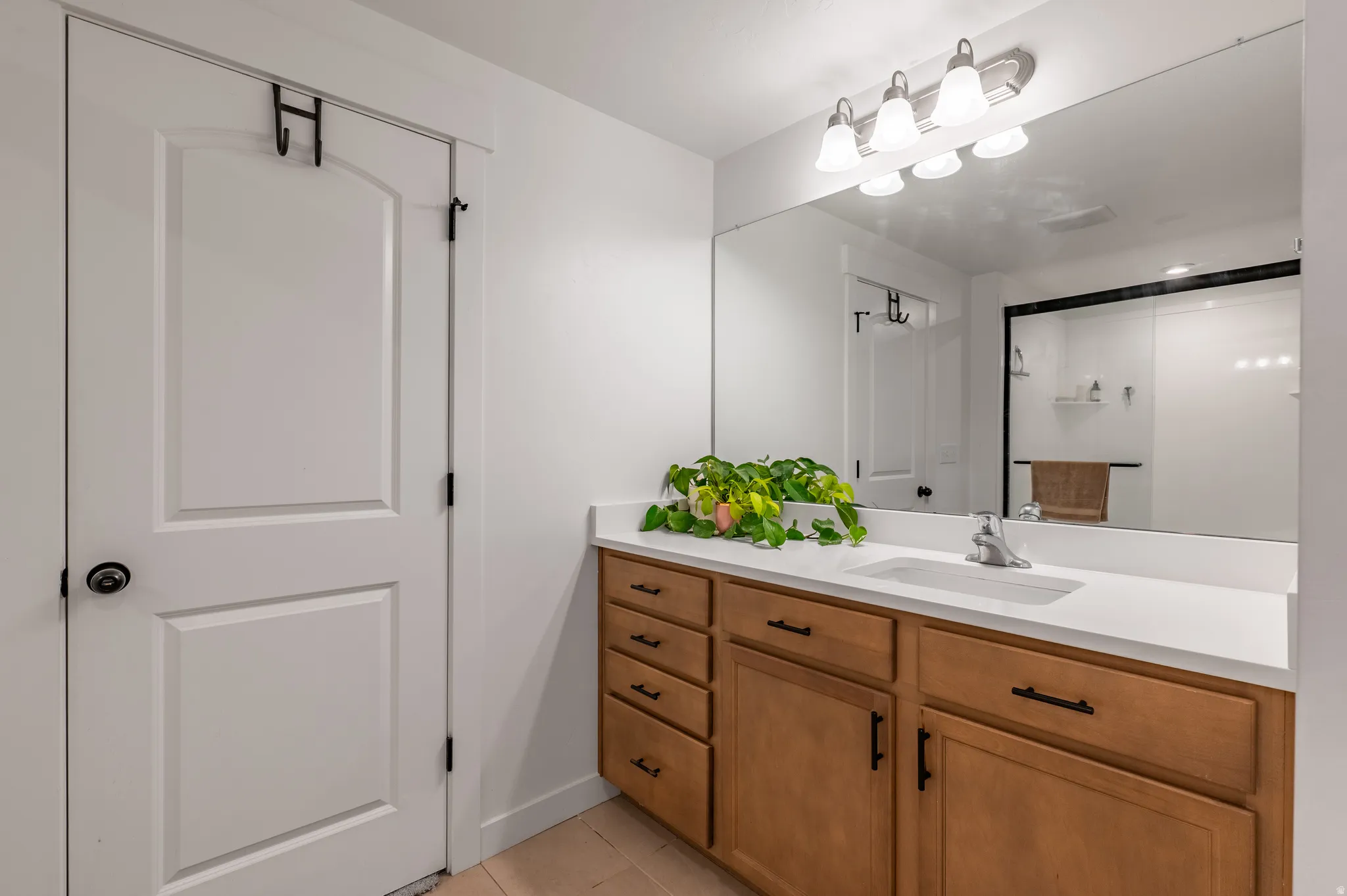 Bathroom vanity with a white countertop and integrated sink, complemented by a large mirror and a four-light fixture