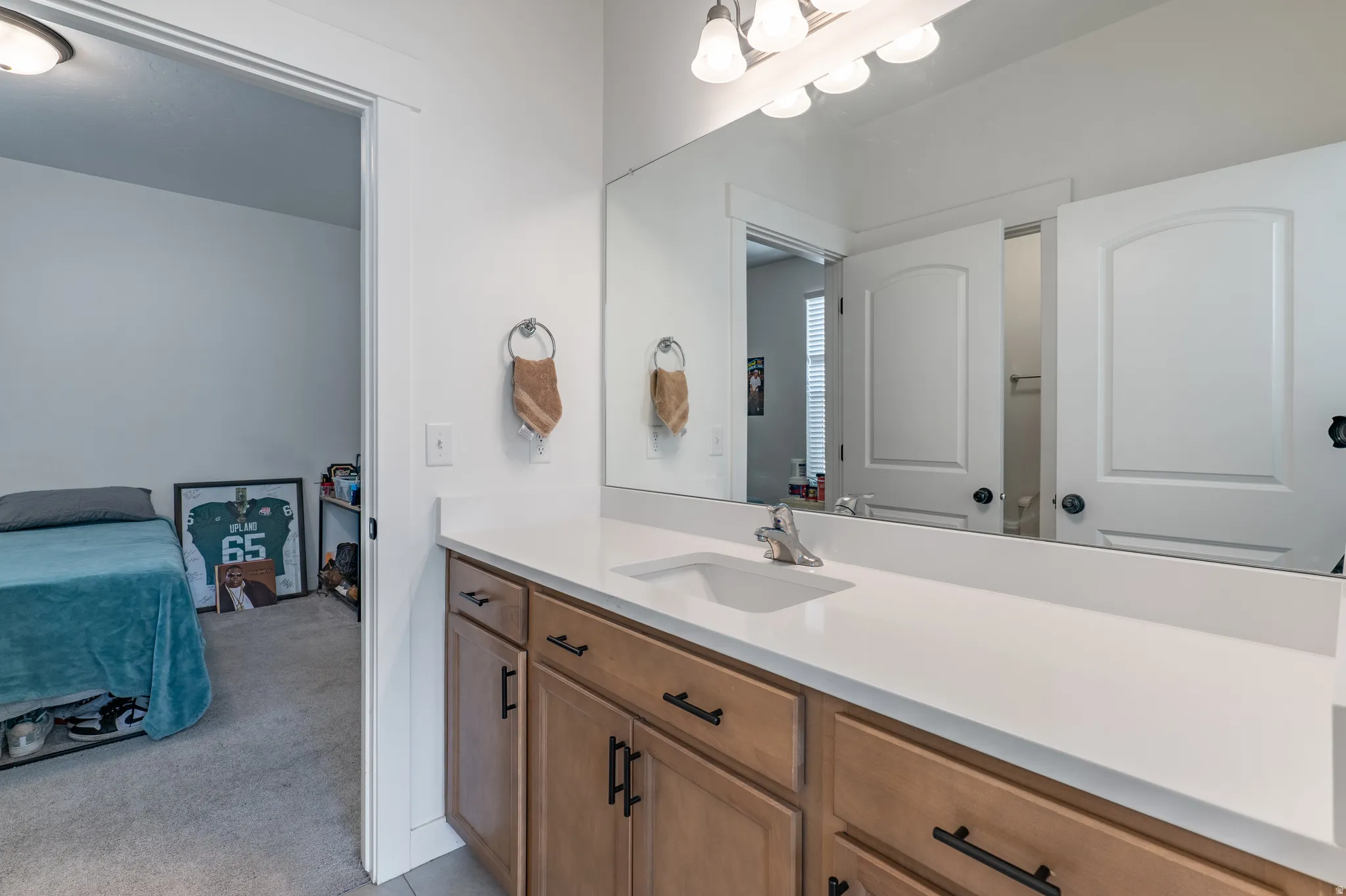 Bathroom vanity featuring light-toned cabinetry, a white countertop with an integrated sink, and an expansive wall-mounted mirror
