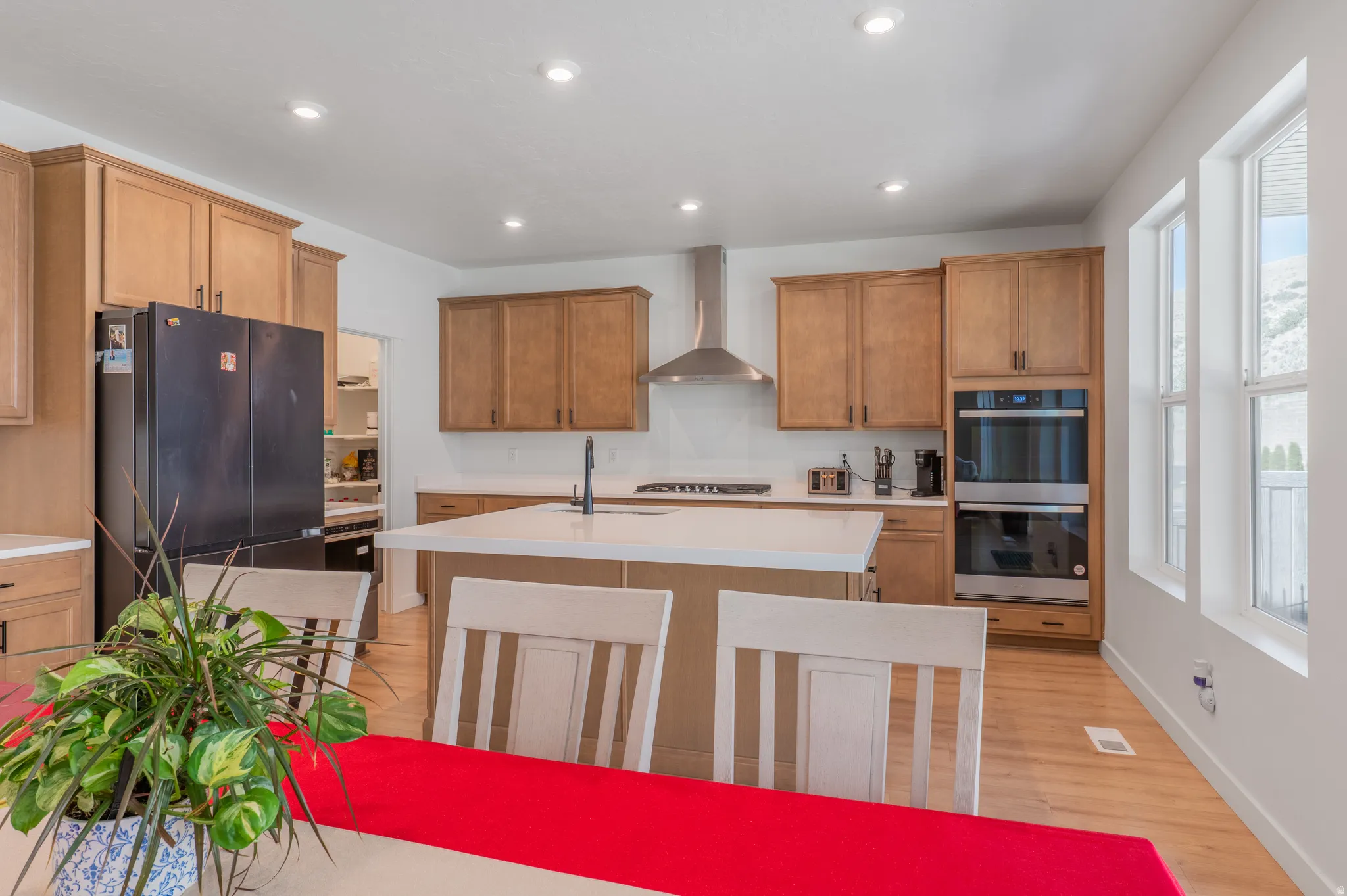 Kitchen featuring light wood cabinetry, a central island with a white countertop, stainless steel double wall ovens, a coordinating stainless steel range hood, and light wood-finish flooring