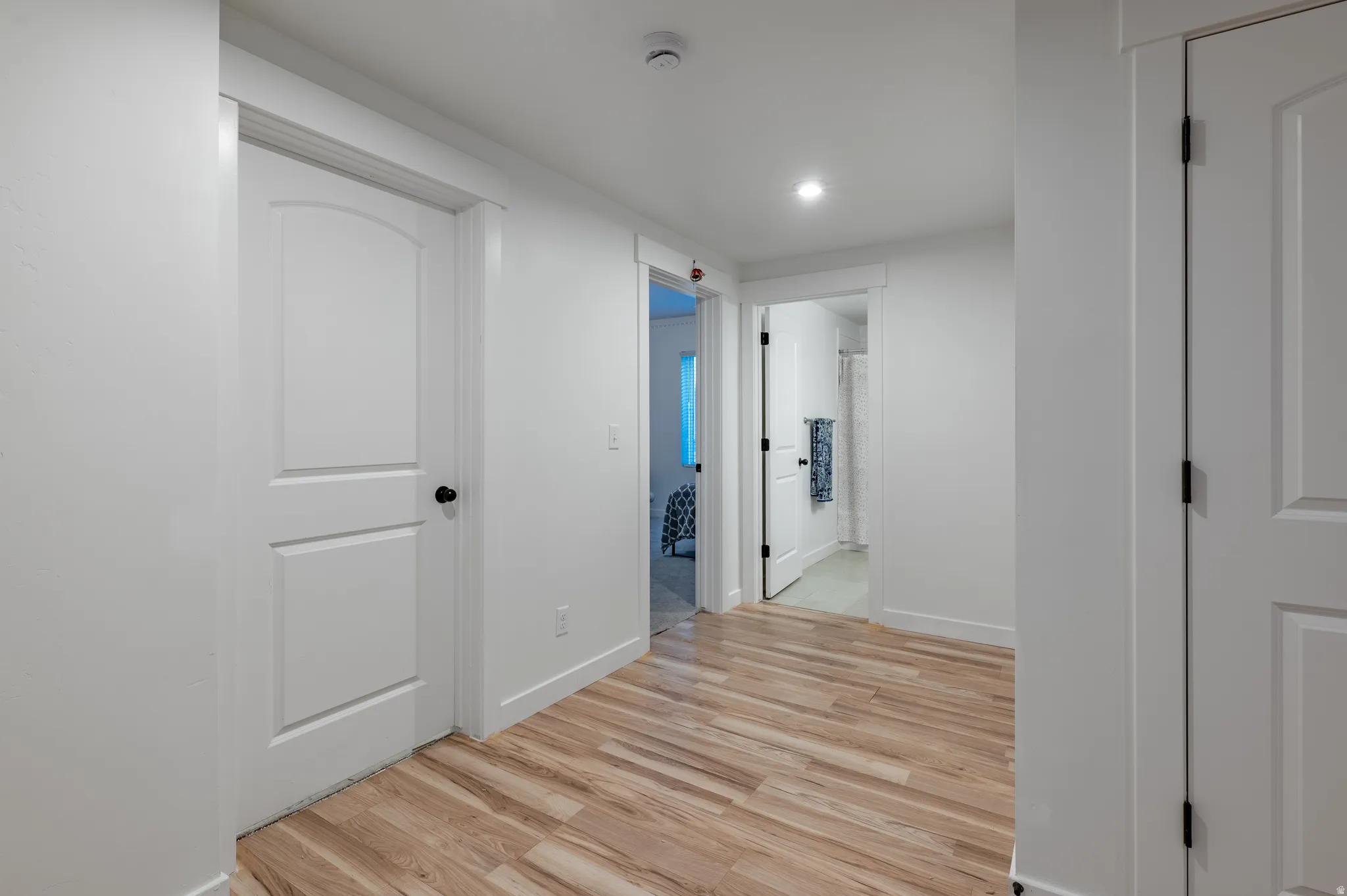 Bright hallway featuring wood-finish flooring, recessed lighting, white walls, and multiple panel doors with black hardware