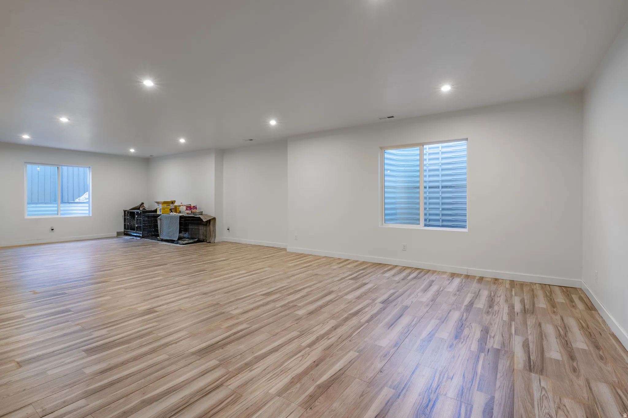 Expansive room with wood-finish flooring, white walls, recessed lighting, and multiple egress windows
