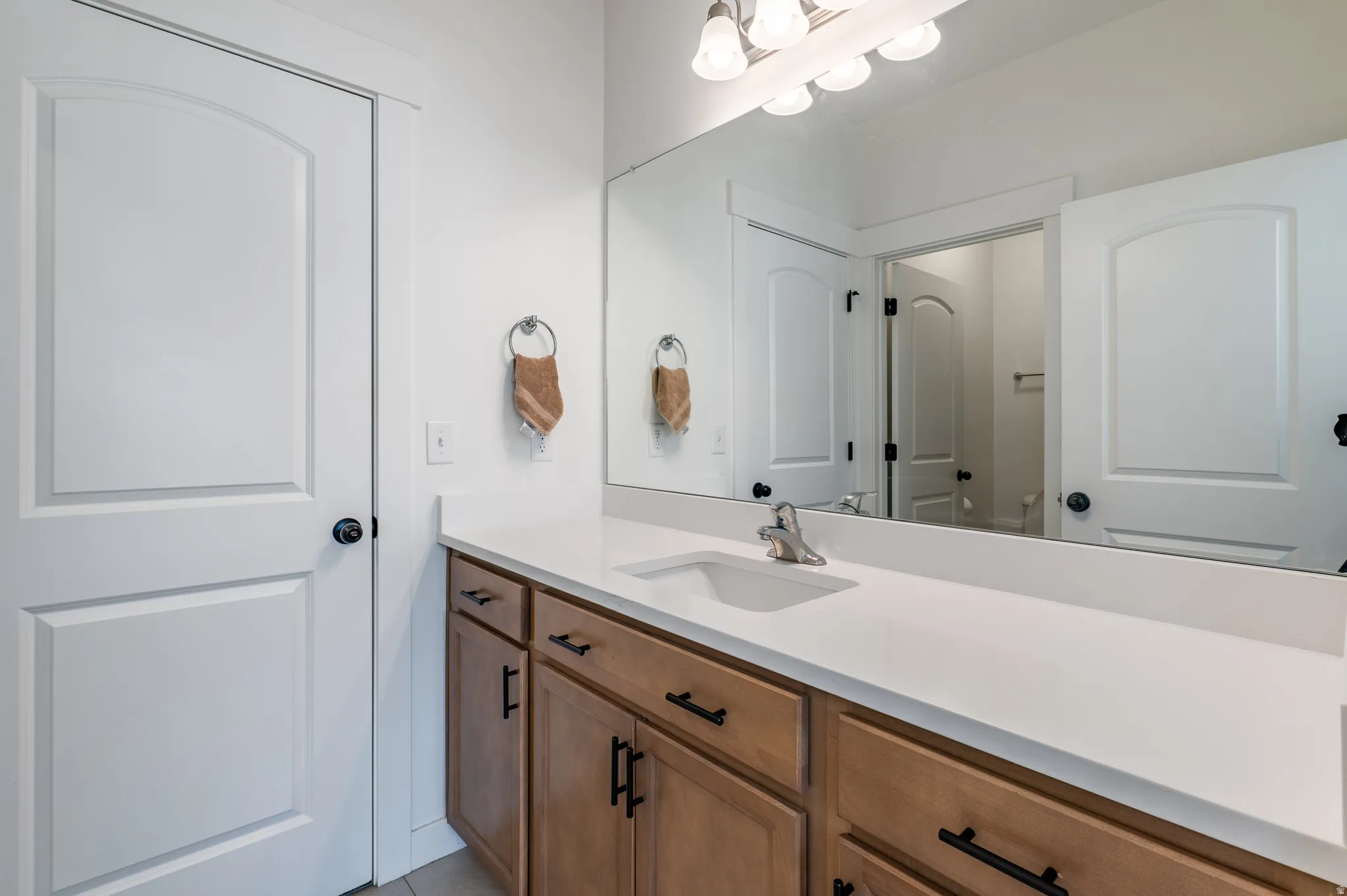 Bathroom vanity featuring a light-toned countertop, wood-finish cabinetry with black hardware, an undermount sink, and a chrome faucet