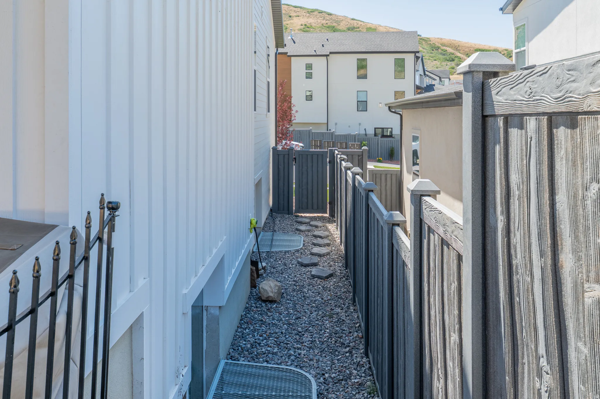Side yard featuring a gravel pathway with stepping stones, bordered by a white vertical siding property wall and a dark wood-finish privacy fence with exit t the front of the house