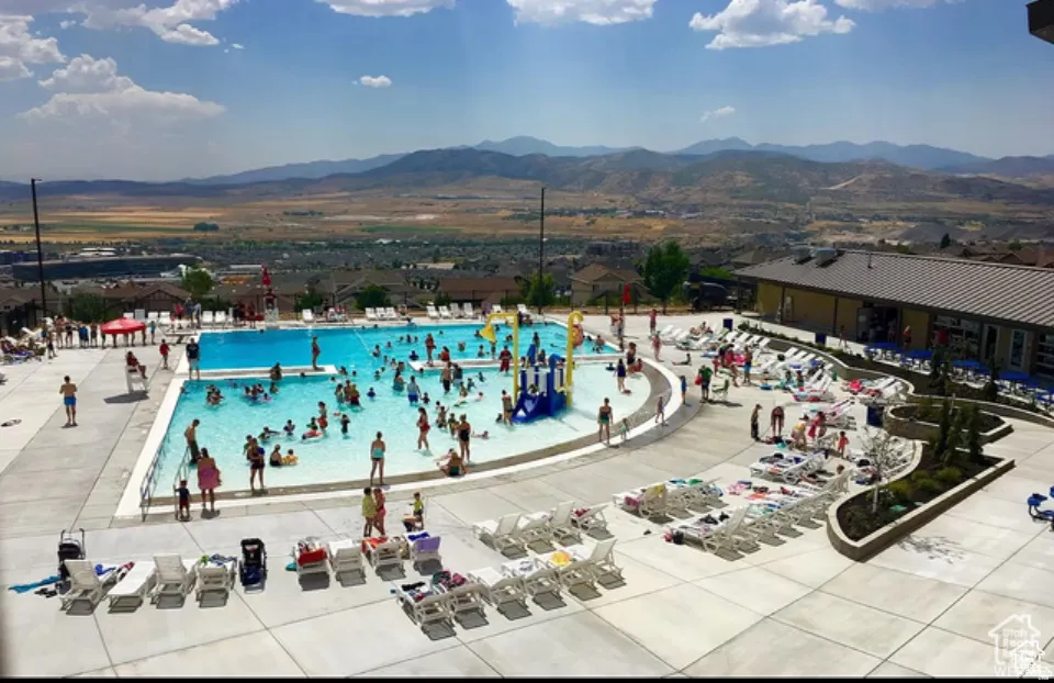 Expansive community pool area featuring a large swimming pool, concrete deck, and adjacent clubhouse building