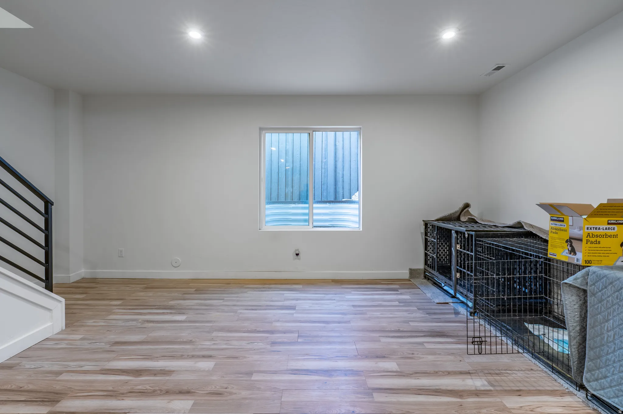 Open finished space featuring wood-finish flooring, recessed lighting, and a white window with a window well