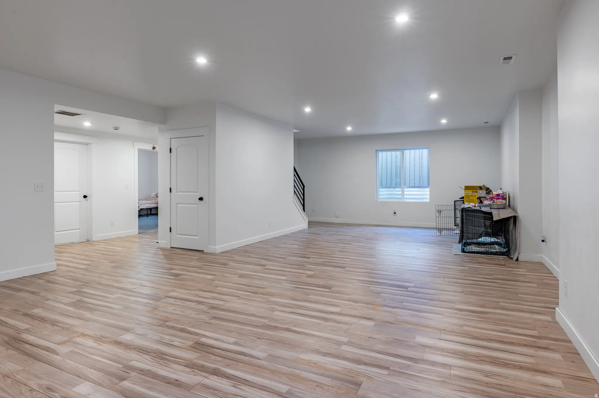 Spacious interior featuring wood-finish flooring, recessed lighting, white walls, and contemporary doors