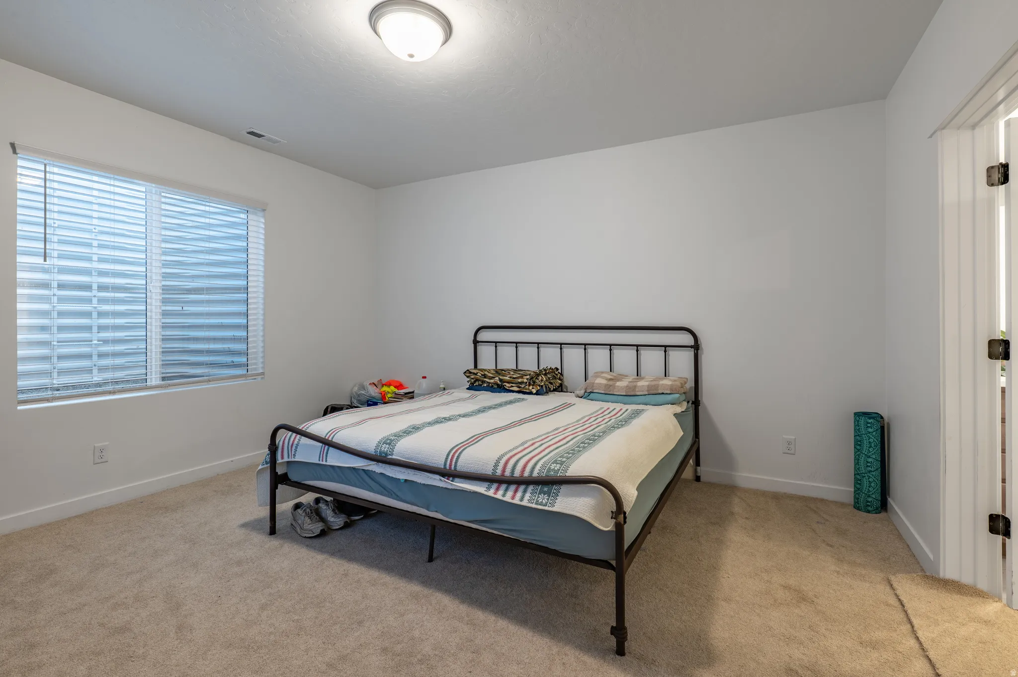 Carpeted room featuring white walls, a single window with blinds, and a flush-mount ceiling light