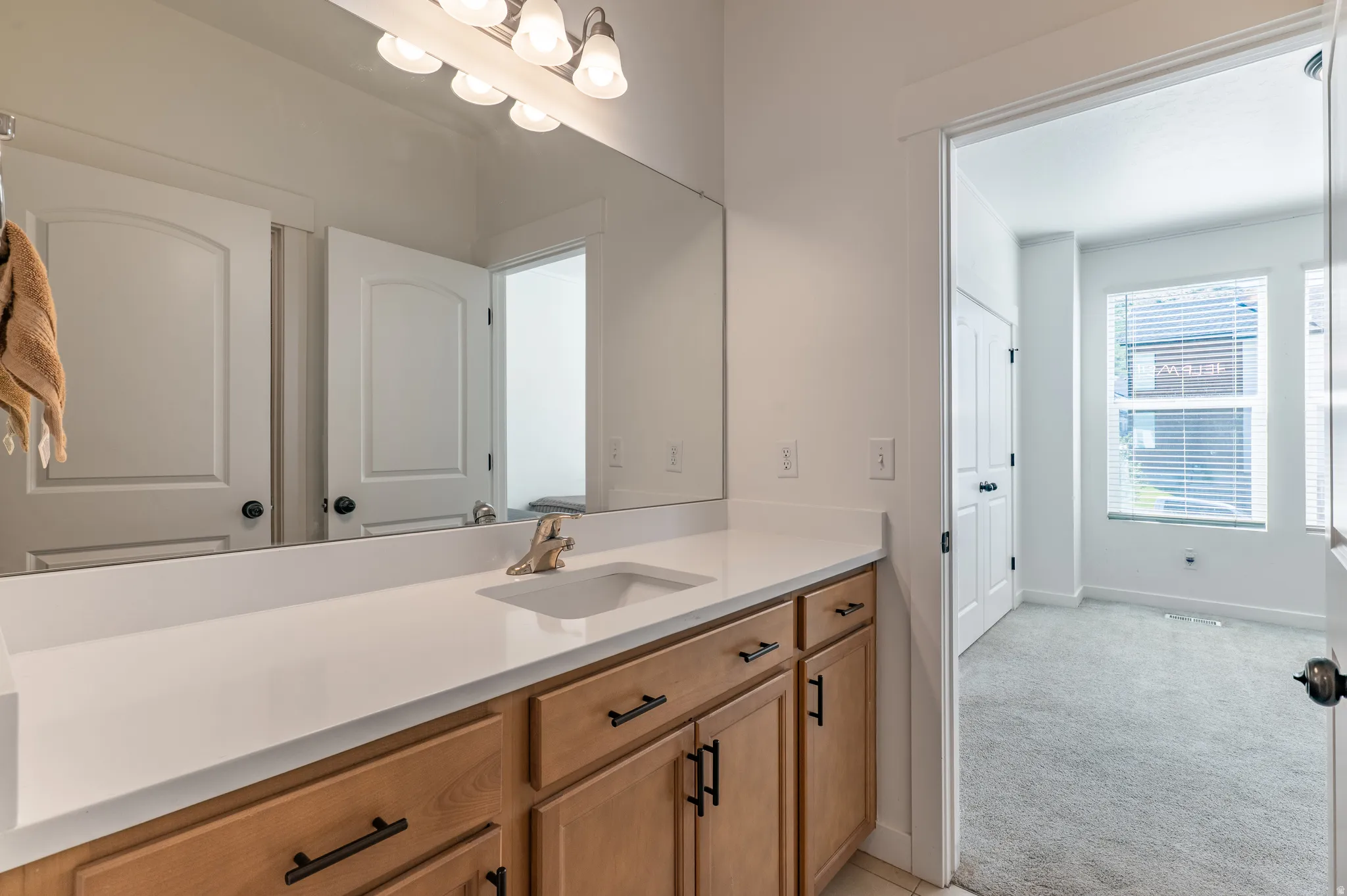 Bathroom vanity featuring a single basin sink, white countertop, wood-finish cabinetry, and matte black hardware