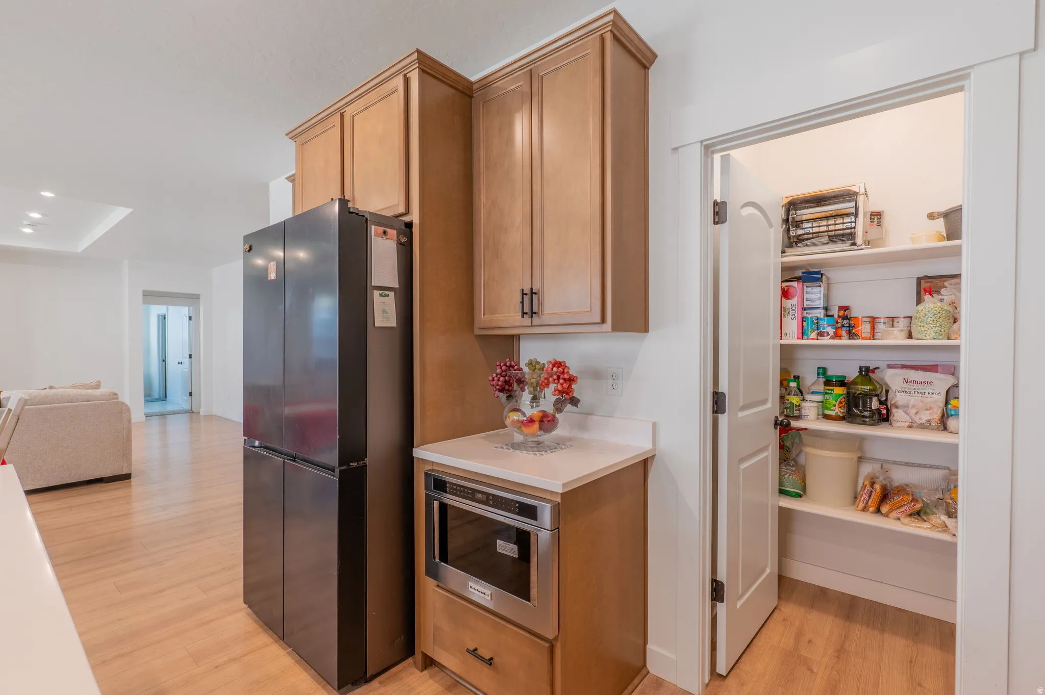 Kitchen area featuring wood-finish flooring, light wood cabinetry with dark hardware, a built-in stainless steel microwave, and white countertops