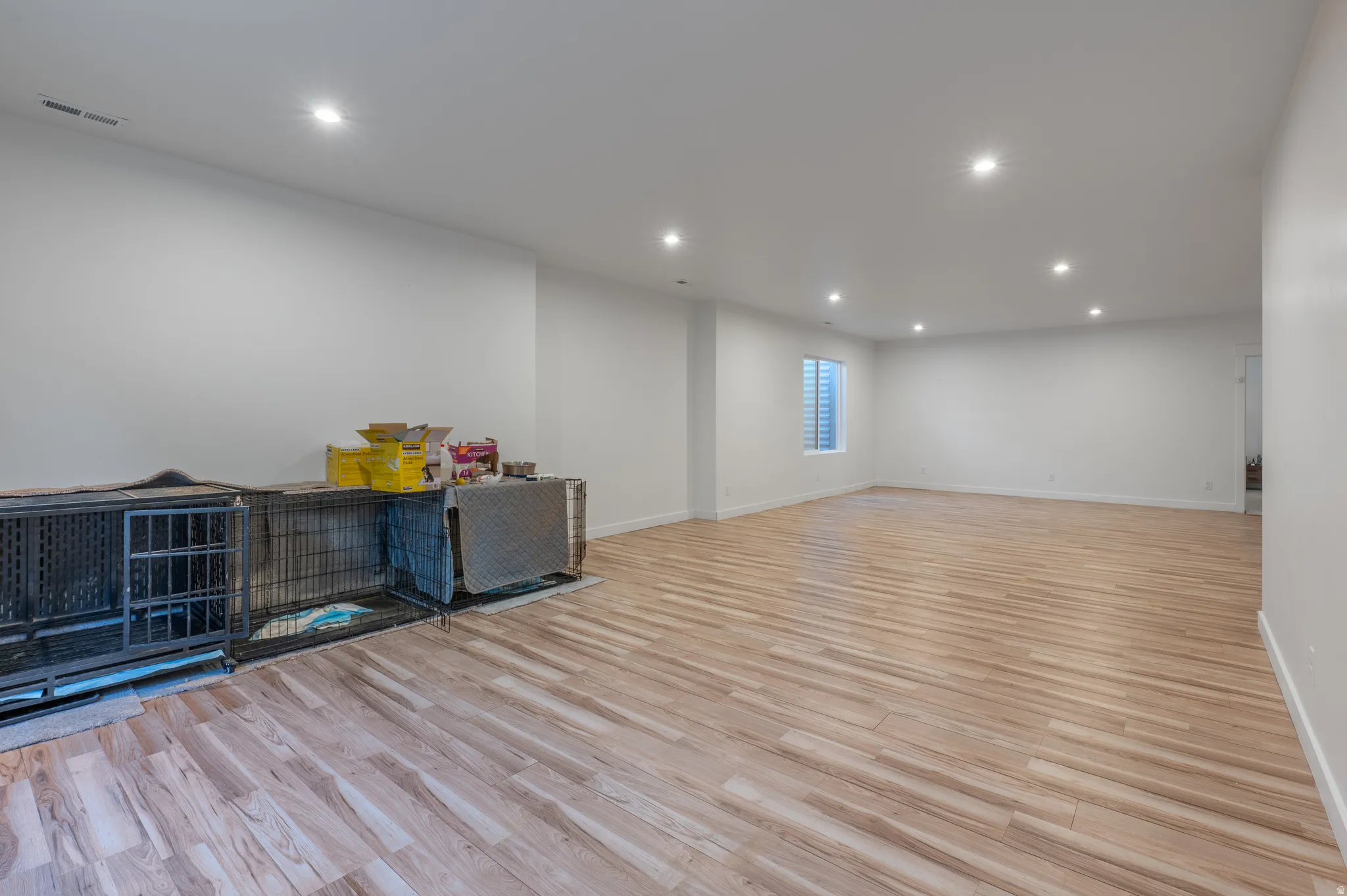 Expansive room featuring wood-finish flooring, recessed ceiling lighting, a single window, and neutral wall finishes