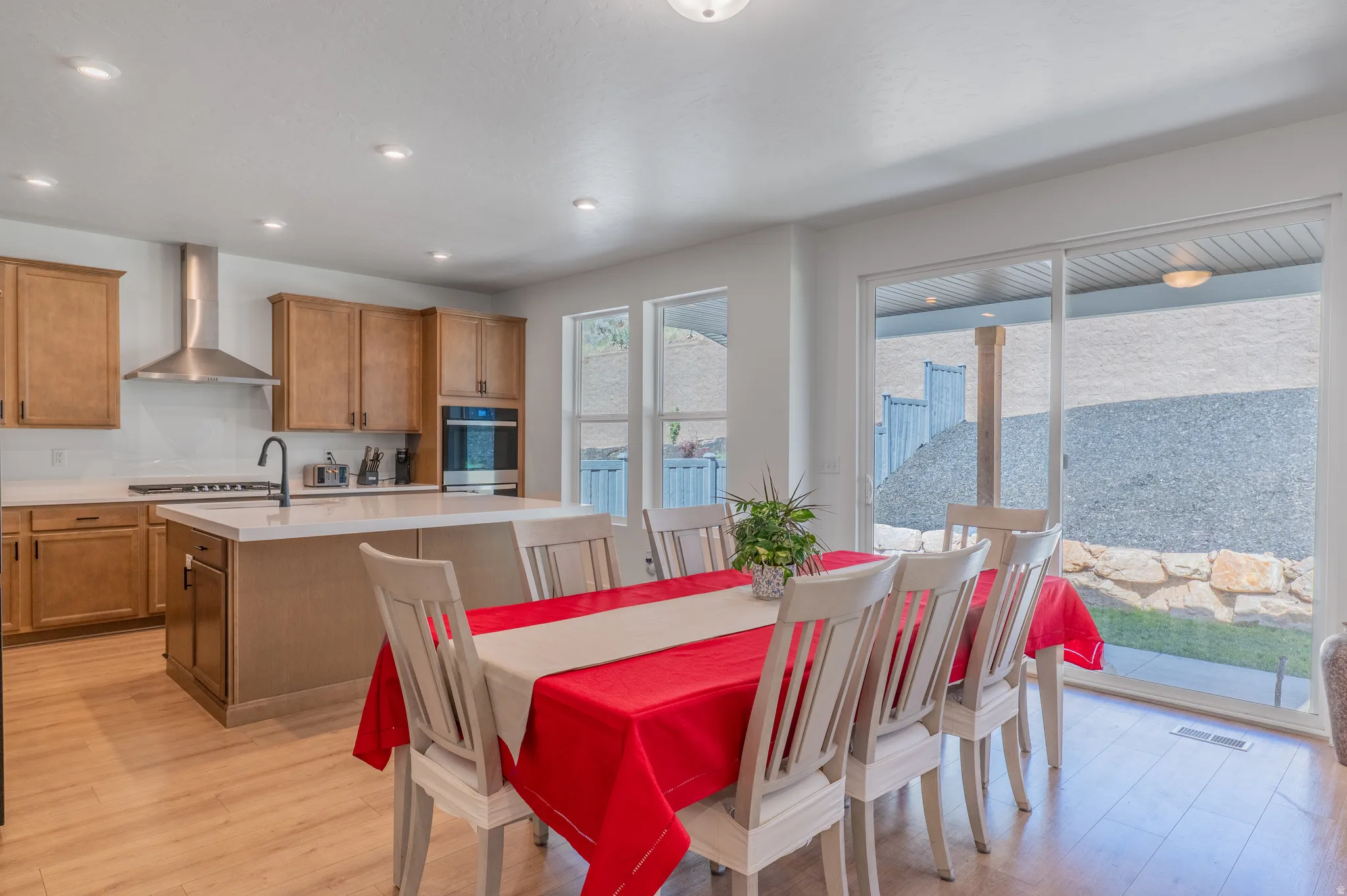 Open-concept kitchen and dining area featuring light wood-finish flooring, a kitchen island with a white countertop, light wood cabinetry, stainless steel appliances, and a sliding glass door providing access to the exterior