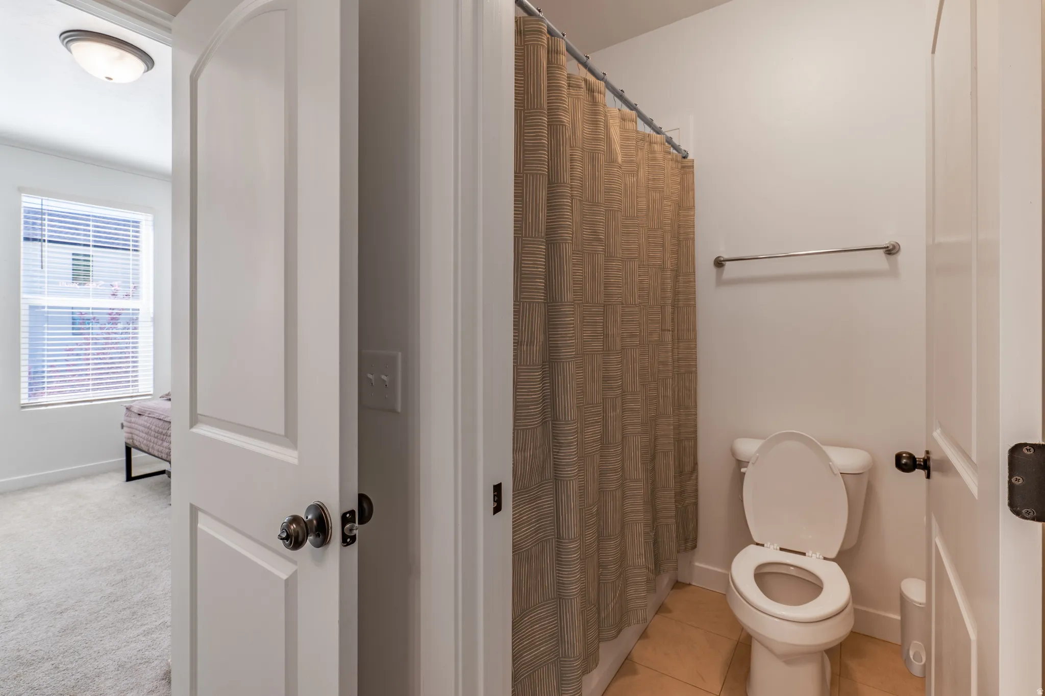 Bathroom with a ceramic tile floor, white toilet, and a chrome towel bar