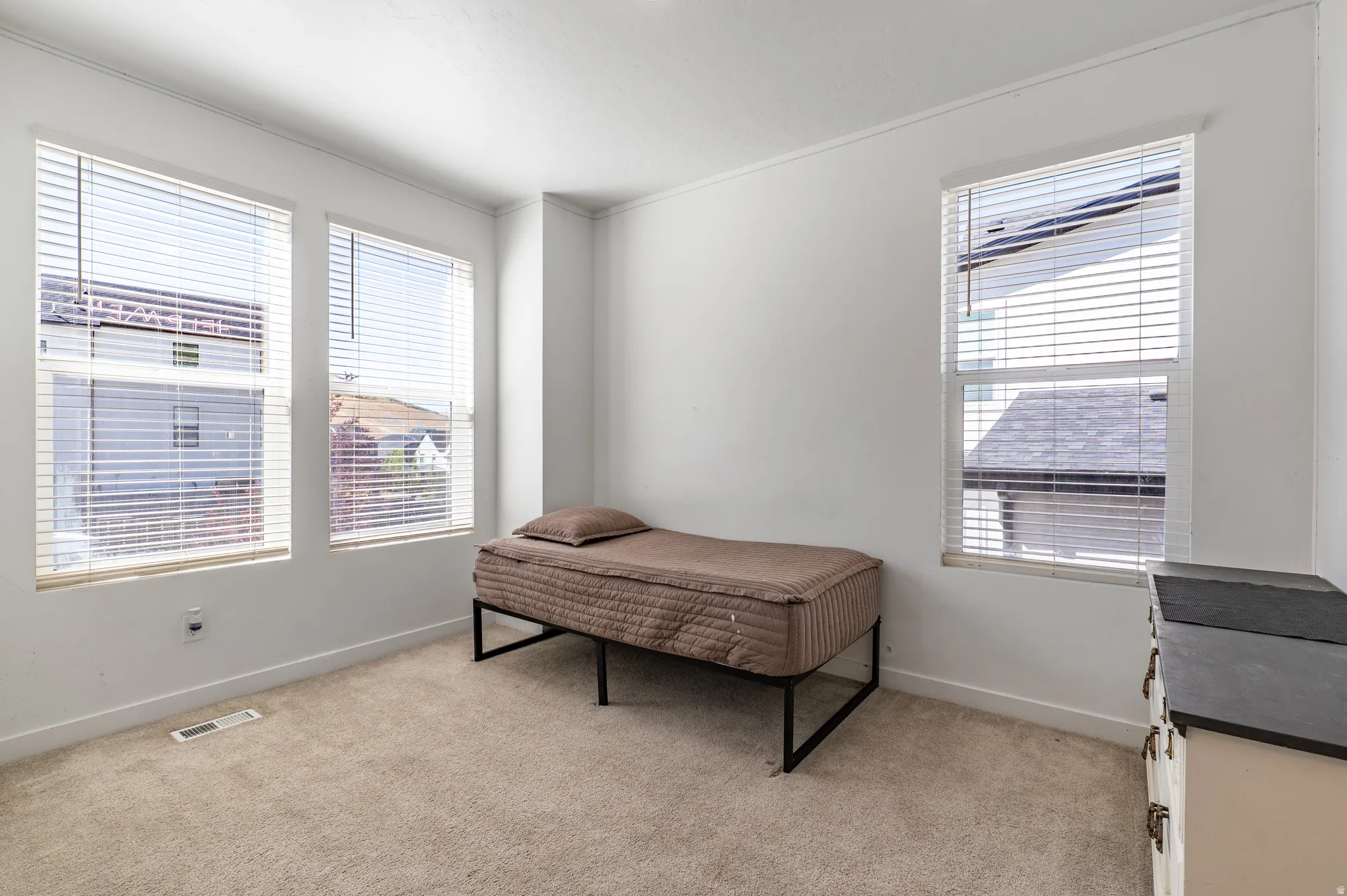 Bright interior space featuring three windows with blinds, light-toned carpeting, white walls, and white baseboards