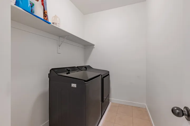 Laundry area featuring a built-in white shelf and neutral tile flooring