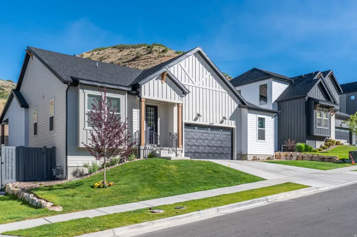 Modern farmhouse exterior featuring vertical white siding, a dark gray garage door, a covered entry with dark wood accents, and a landscaped front yard with a tree
