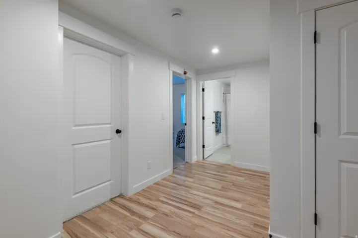 Bright hallway featuring wood-finish flooring, recessed lighting, white walls, and multiple panel doors with black hardware