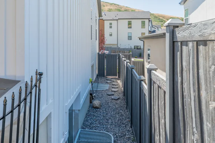 Side yard featuring a gravel pathway with stepping stones, bordered by a white vertical siding property wall and a dark wood-finish privacy fence with exit t the front of the house