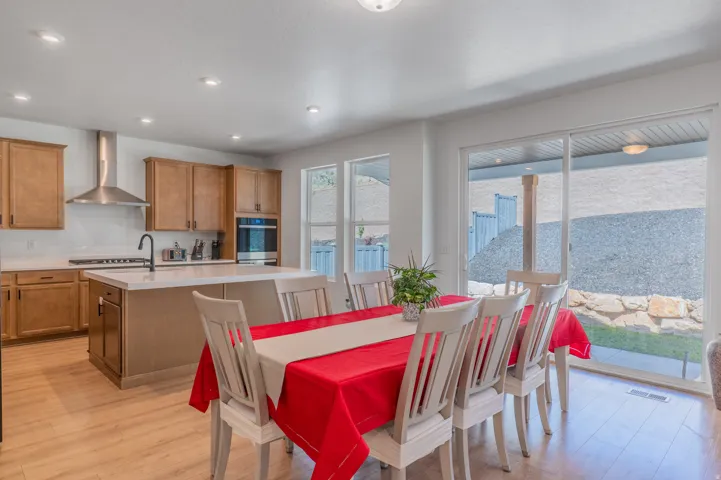 Open-concept kitchen and dining area featuring light wood-finish flooring, a kitchen island with a white countertop, light wood cabinetry, stainless steel appliances, and a sliding glass door providing access to the exterior