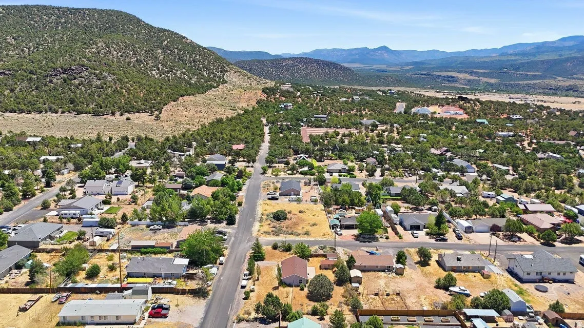 Aerial panorama showcasing a residential community nestled against a tree-covered hillside, with distant mountains forming a natural backdrop