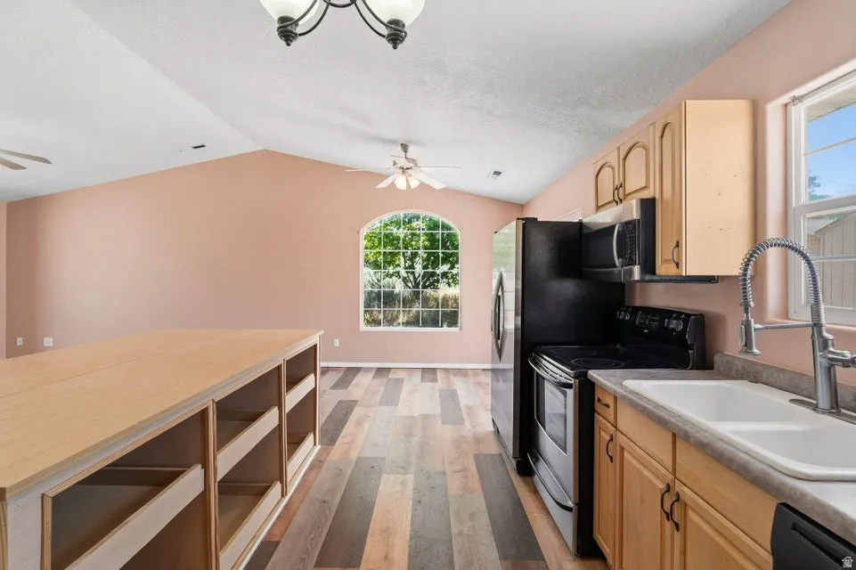 Kitchen featuring light wood-finish cabinetry, black appliances, and a double basin sink with a high-arch faucet