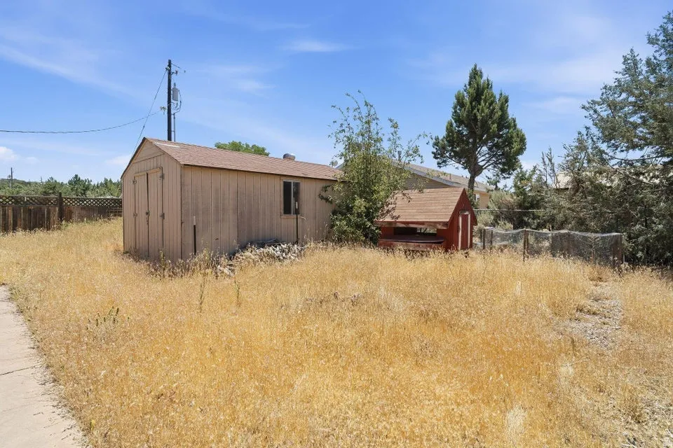 Spacious outdoor area featuring a large utility shed with double doors and a window, a smaller red-painted structure, and a perimeter fence