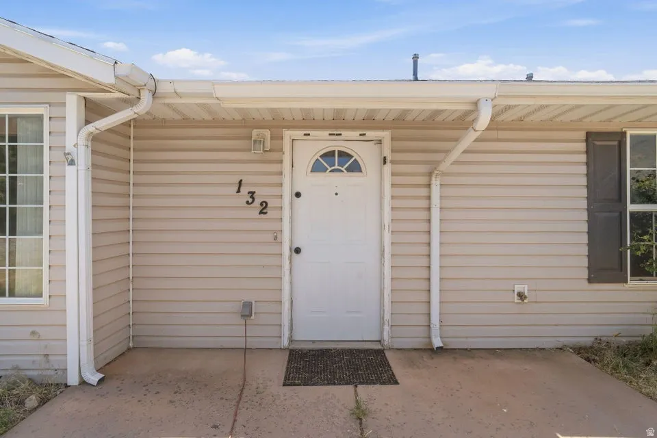 Neutral-toned horizontal siding facade featuring a white entry door with an arched transom window, black address numbers, and a covered concrete porch