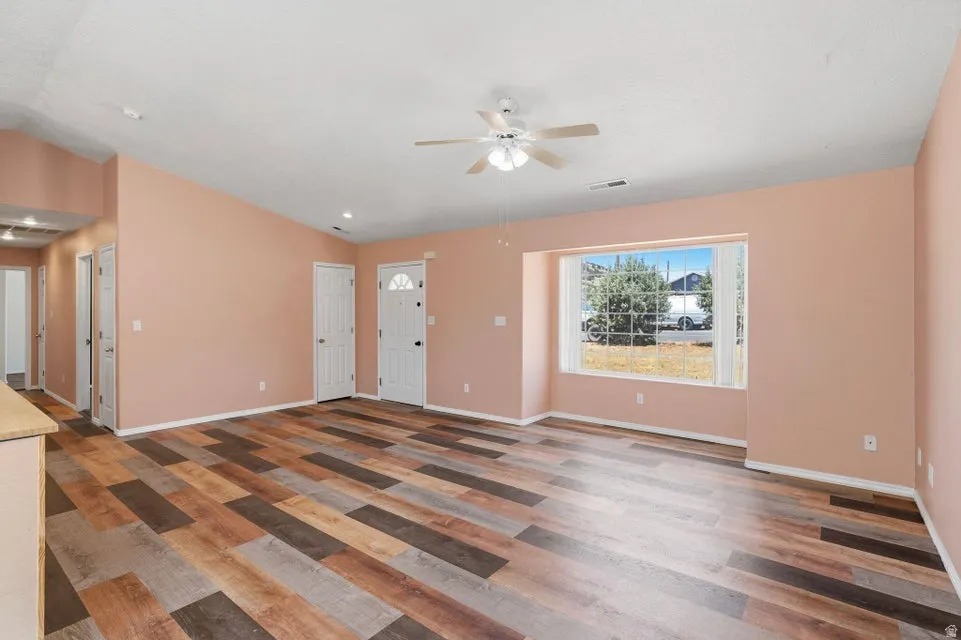 Spacious room featuring multi-toned wood-finish flooring, a contemporary ceiling fan, and a large bay window