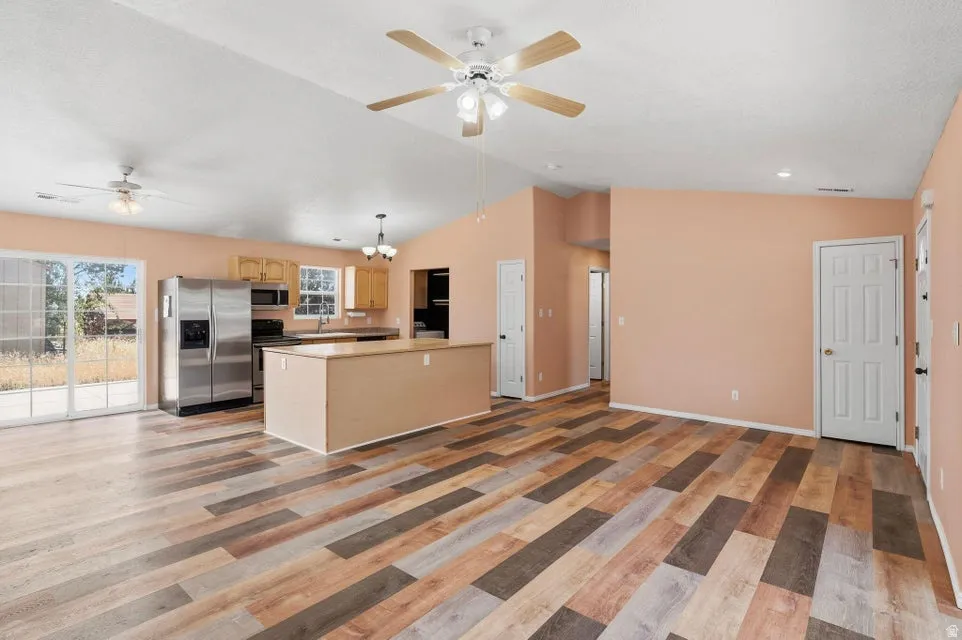 Expansive living area featuring multi-tone wood-finish flooring, vaulted ceilings, and ceiling fan light fixtures