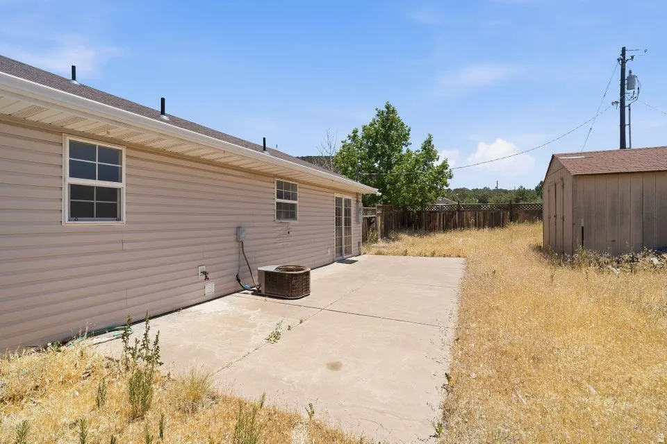Rear exterior featuring beige horizontal siding, a concrete patio, and a separate storage shed with a shingle roof