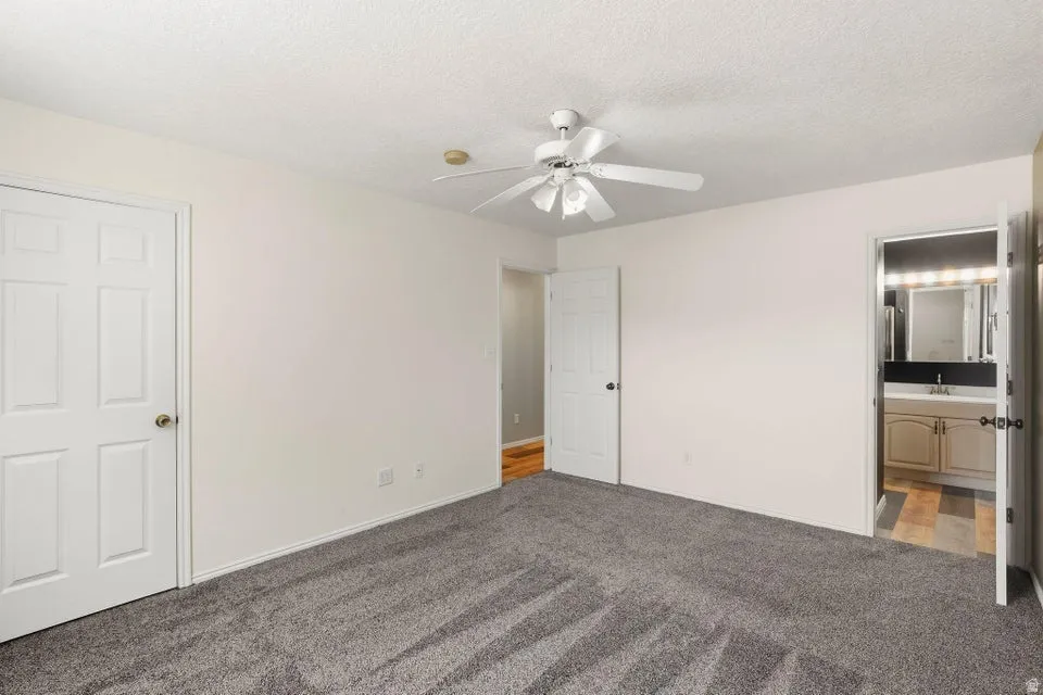 Spacious room featuring gray textured carpeting, a white ceiling fan, and white interior doors