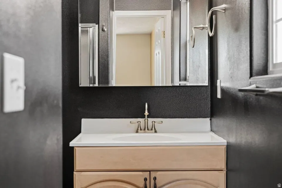 Bathroom vanity with a light wood-finish cabinet, white countertop, and brushed nickel faucet