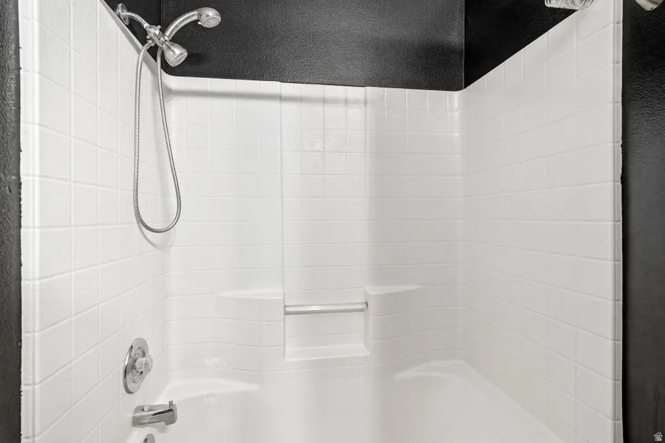 White tiled shower-tub combination featuring a handheld showerhead and built-in shelving