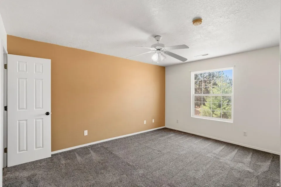 Carpeted interior room with a paneled door, a single window, and a ceiling fan with integrated lighting
