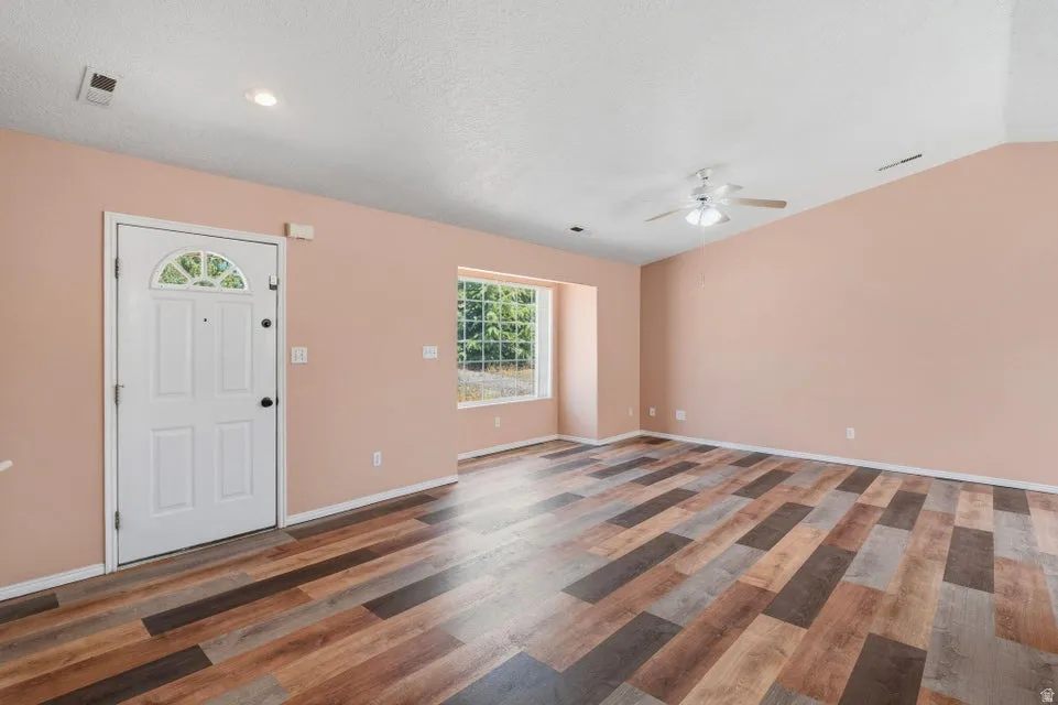 Spacious room featuring multi-tone wood-finish flooring, a vaulted ceiling with a ceiling fan, and recessed lighting