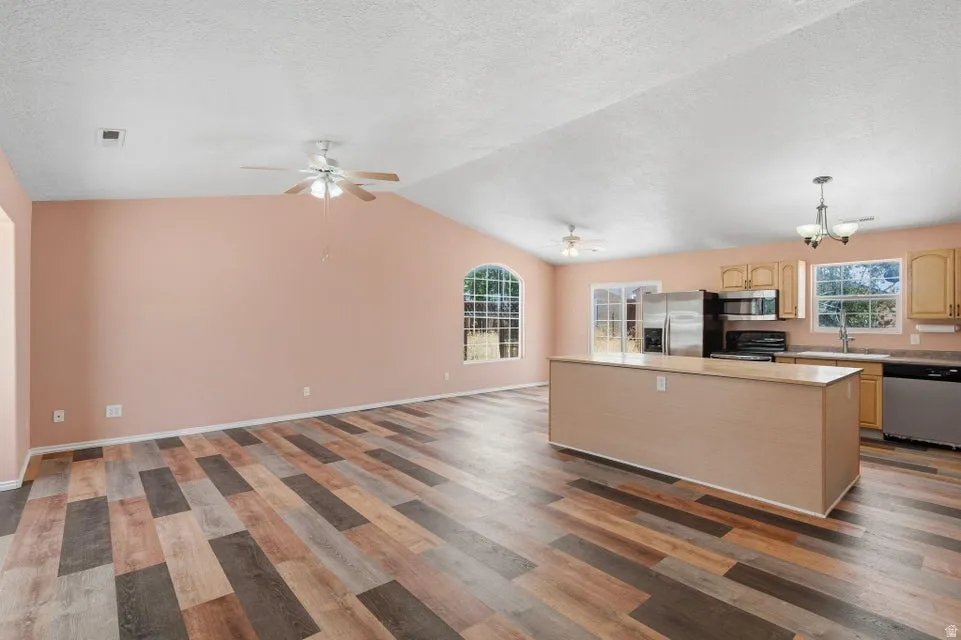 Spacious open-concept interior featuring vaulted ceilings, wood-finish flooring, and a kitchen island