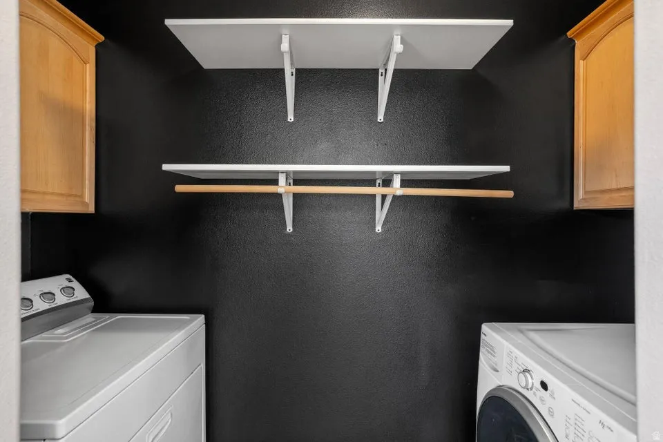 Laundry area featuring two white shelving units, a wooden hanging rod, and two light wood-finish wall cabinets