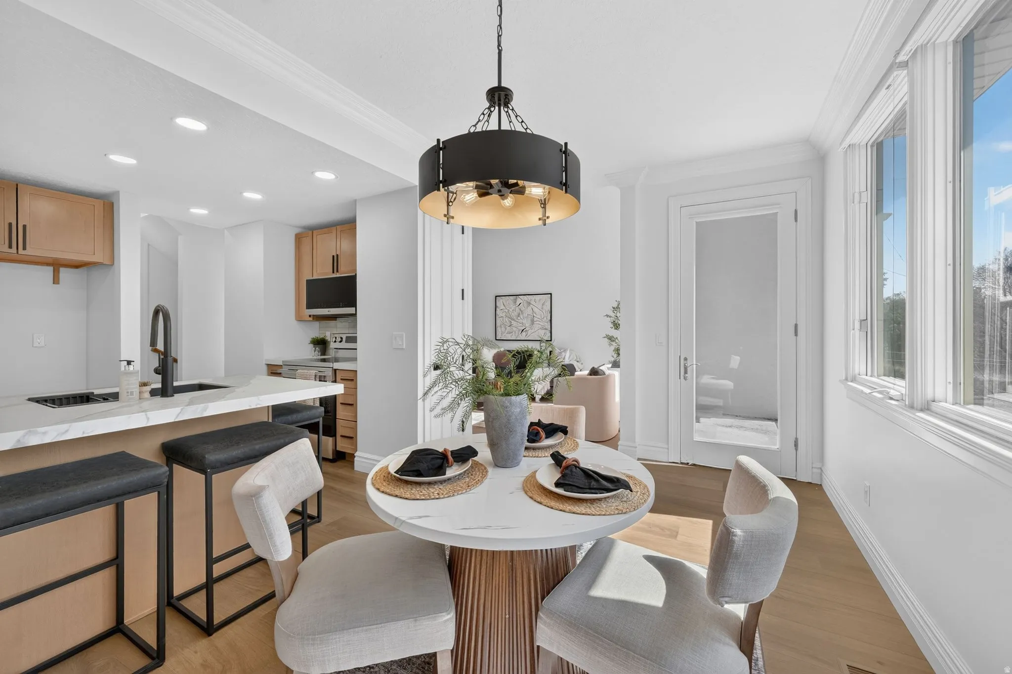 Open-concept dining area featuring a contemporary pendant light fixture, wood-finish flooring, and crown molding
