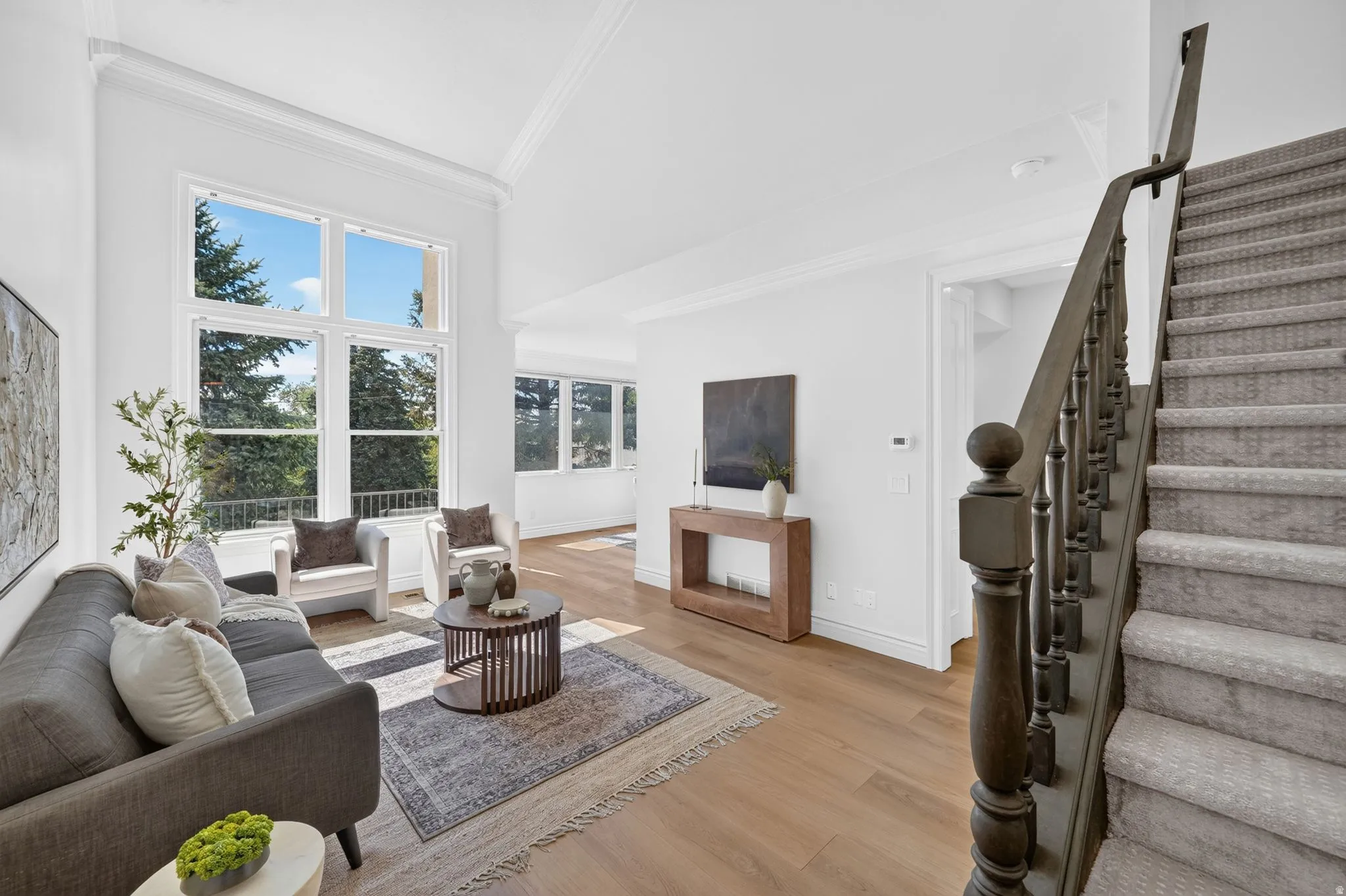 Living space featuring soaring ceilings, a double-height window, wood-finish flooring, a carpeted staircase with wood banister, and crown molding