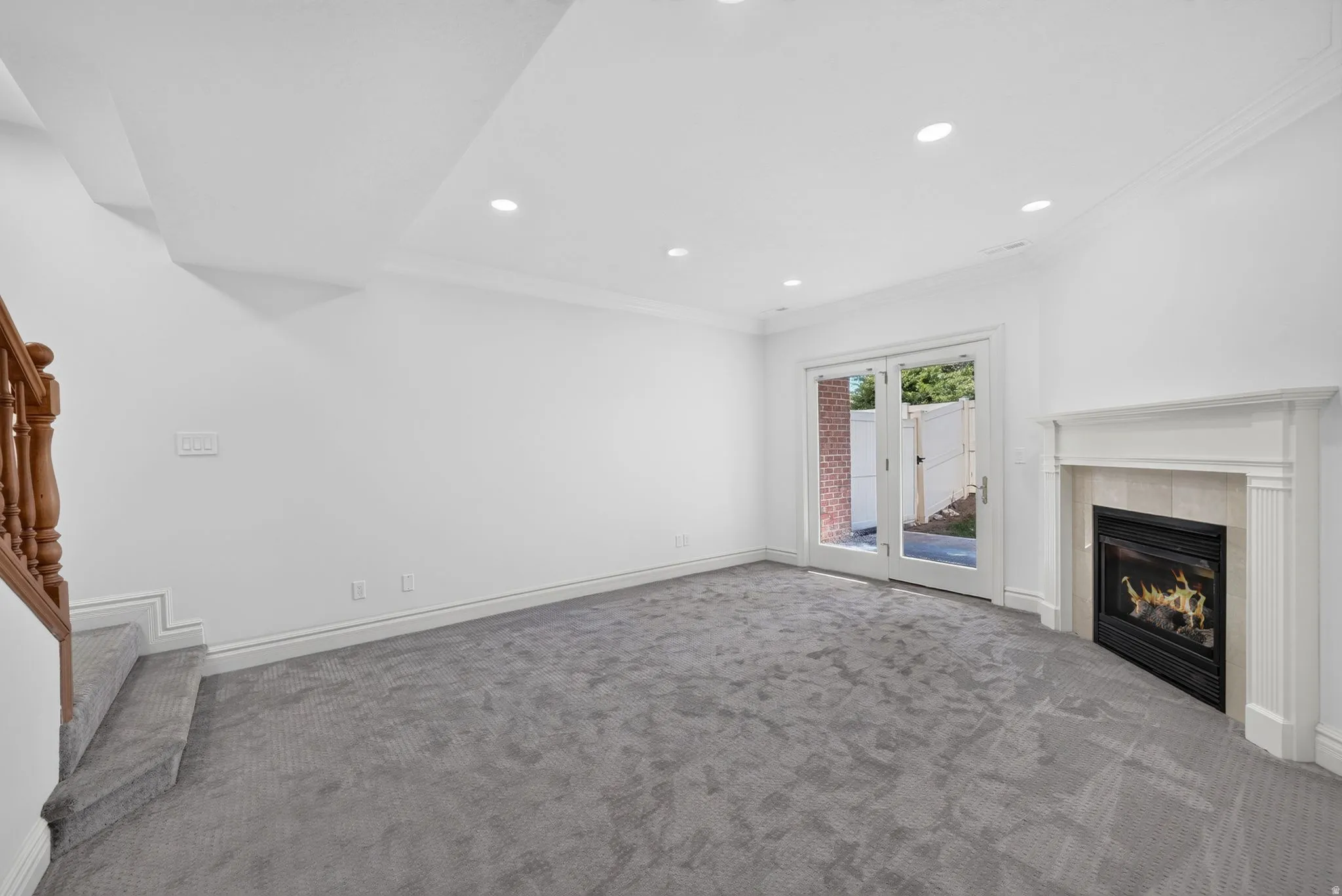 Spacious room featuring gray carpeting, recessed lighting, white crown molding, and a fireplace with a light-colored tile surround and white mantel