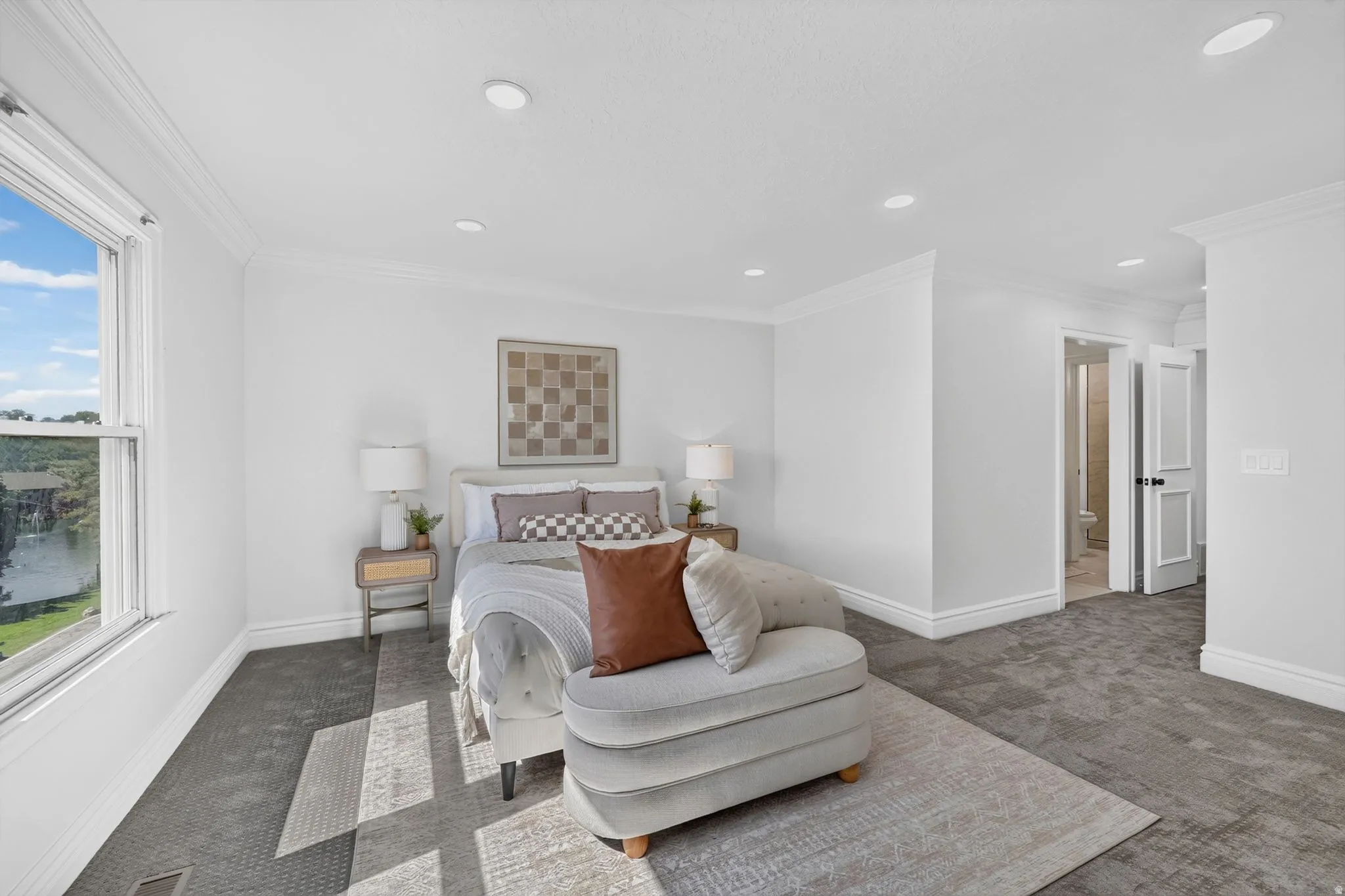 Spacious room with white walls and crown molding, featuring recessed lighting and a large window overlooking a body of water and green landscape
