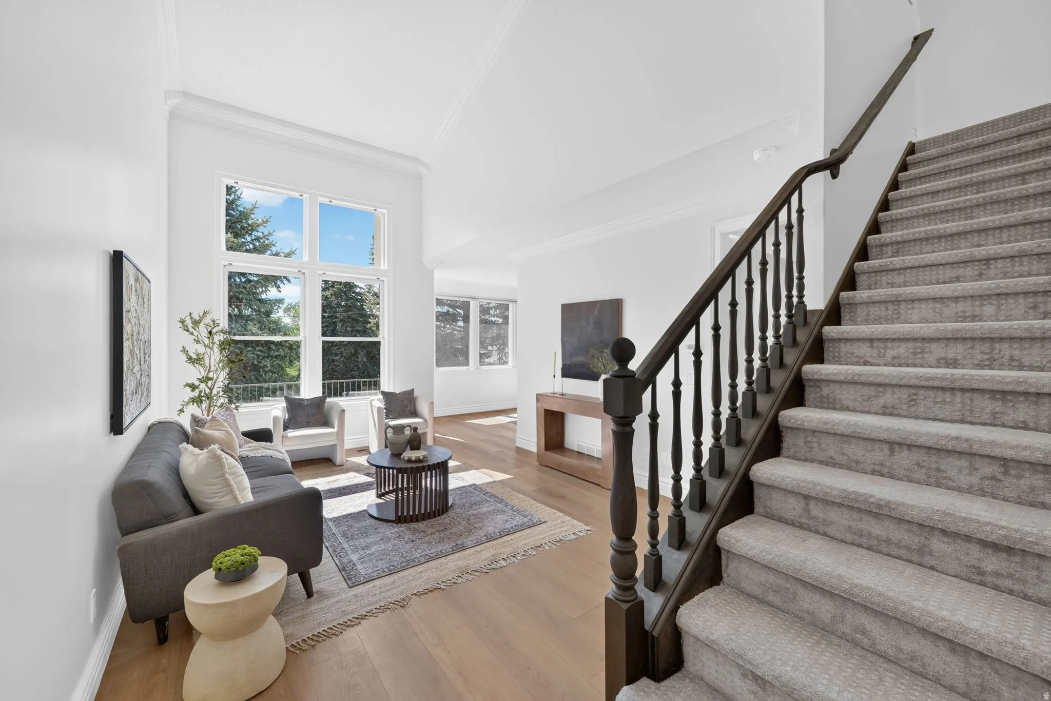 Two-story living area featuring tall windows, light wood-finish flooring, white walls, and crown molding