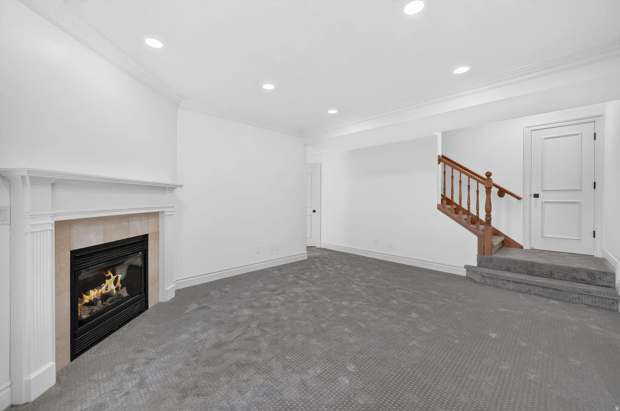 Carpeted room featuring a fireplace with a stone surround and white mantel, recessed lighting, crown molding, and a staircase with a wood handrail