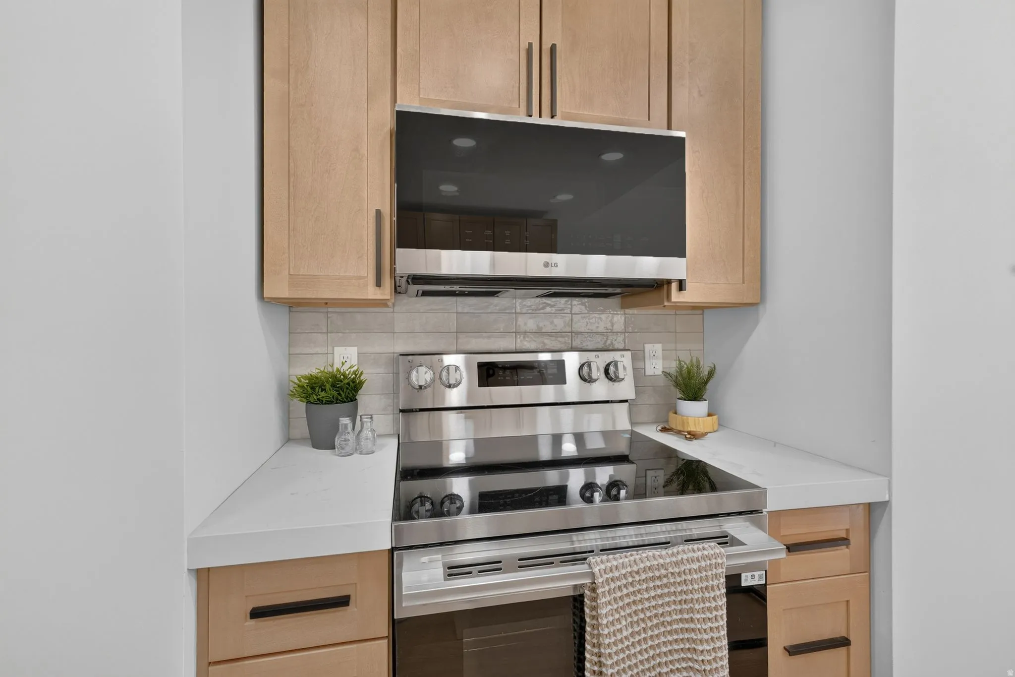 Kitchen featuring light wood-finish cabinetry, stainless steel oven and microwave, white countertops, and a gray tile backsplash