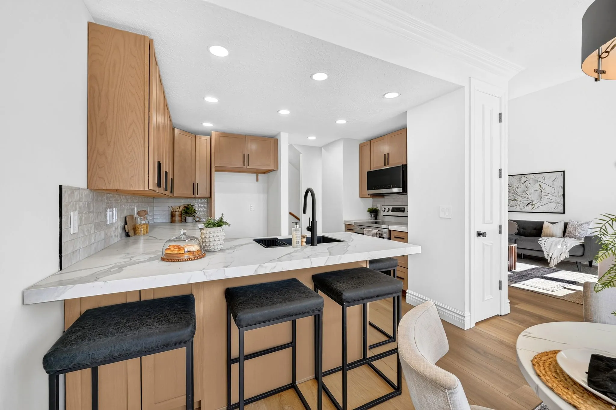 Kitchen featuring light wood-finish cabinetry with matte black hardware, white stone-finish countertops, and a subway tile backsplash