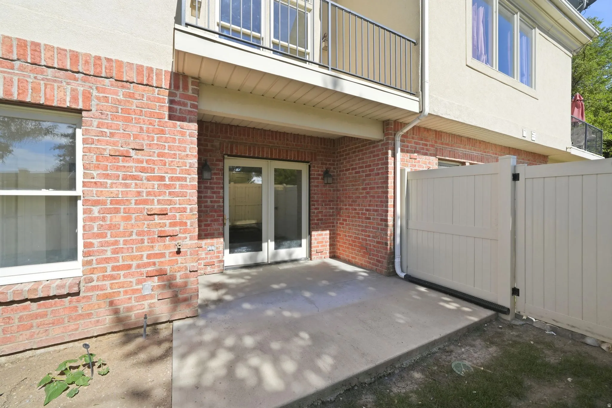 Paved patio area featuring red brick and stucco exterior, white framed glass French doors, and a private perimeter fence