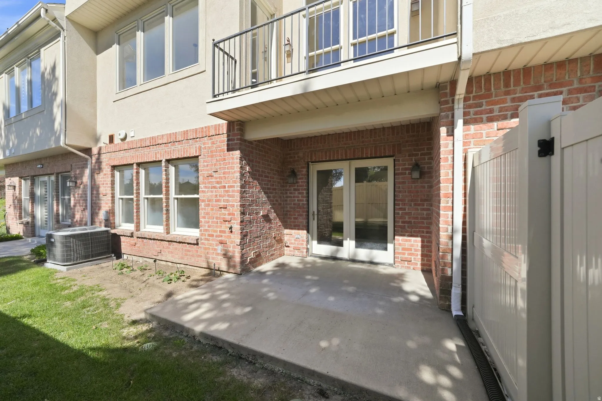 Ground-level patio featuring concrete slab, brick siding, and double French doors with transom windows