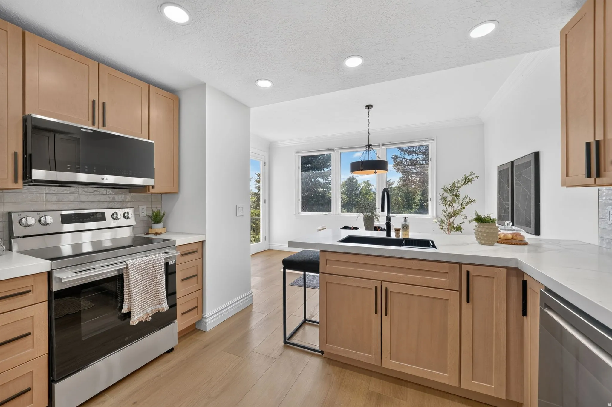 Modern kitchen featuring light wood cabinetry with black hardware, stainless steel appliances, and light-toned countertops
