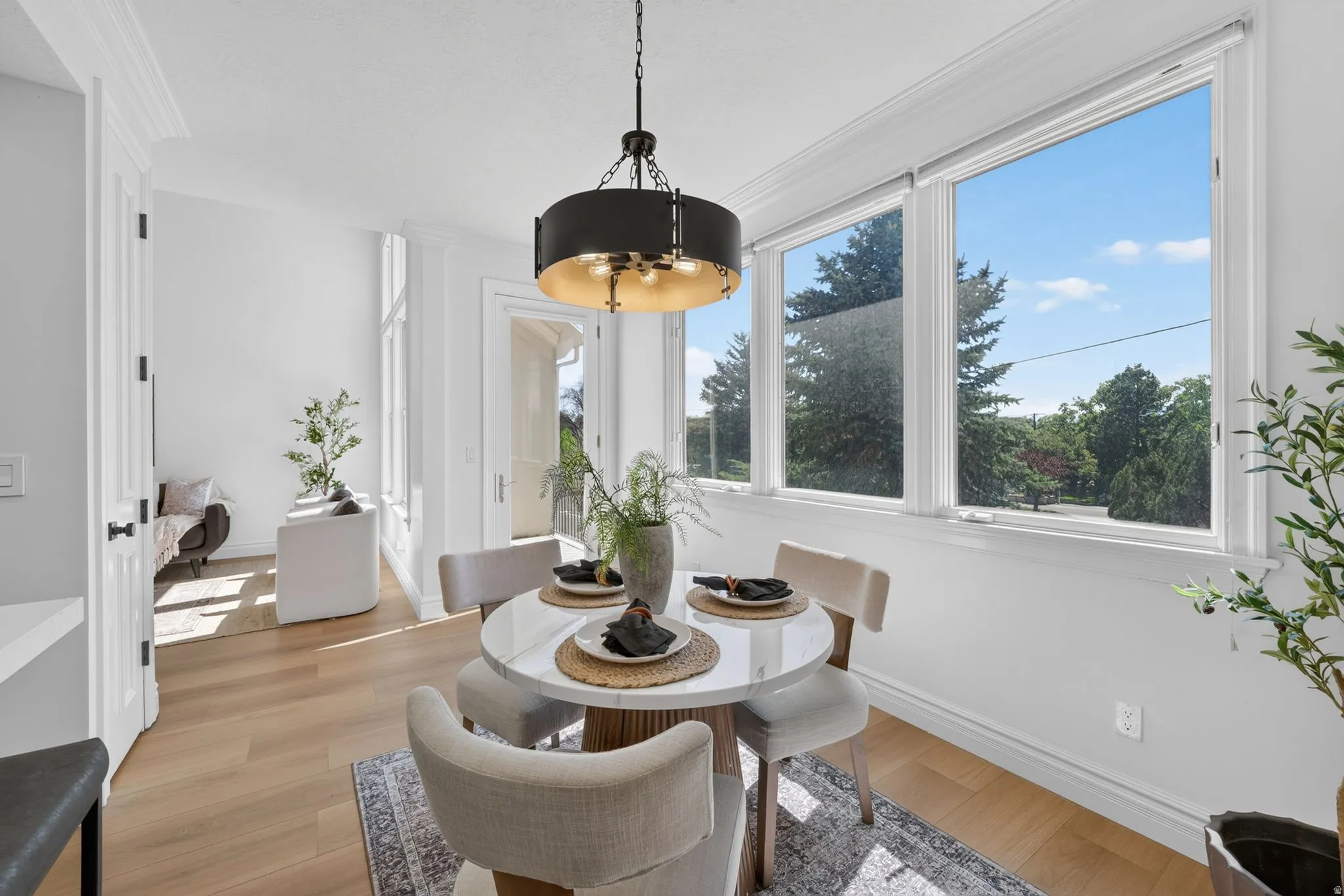 Dining area featuring a contemporary chandelier, large windows, light wood-finish flooring, and white walls with crown molding