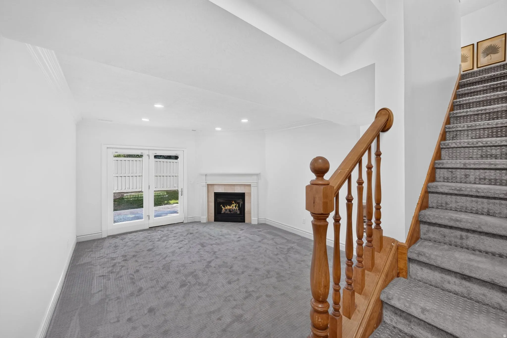 Spacious room featuring gray textured carpet, a fireplace with a stone mantel, and double glass-paneled doors
