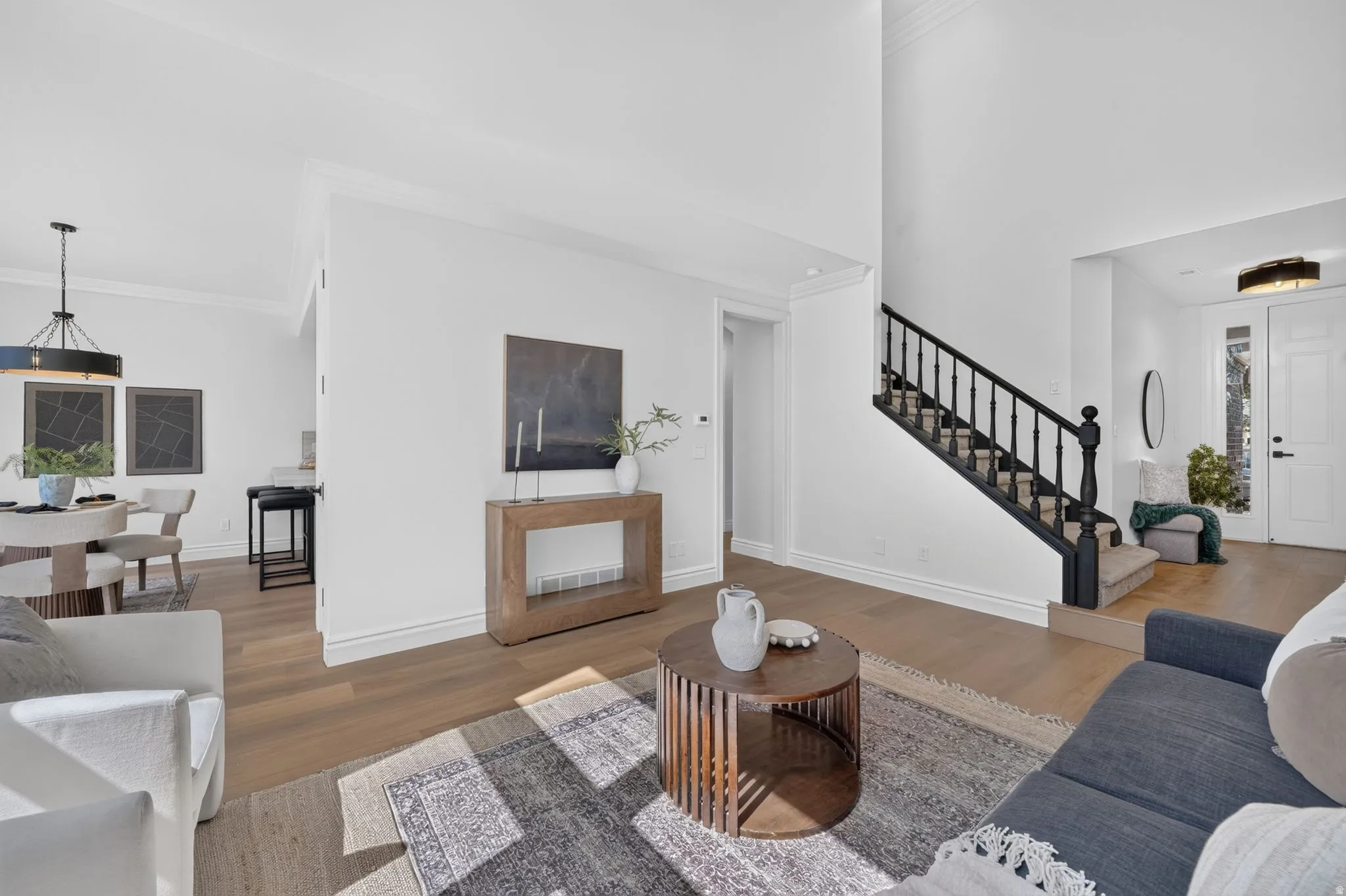 Expansive living area featuring wood-finish flooring, a contemporary black banister staircase, bright white wall finishes, and crown molding